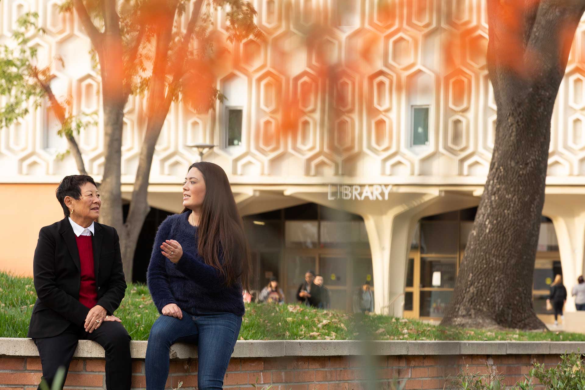 Janice Jeng and Ginny Oshiro sit and talk in front of library